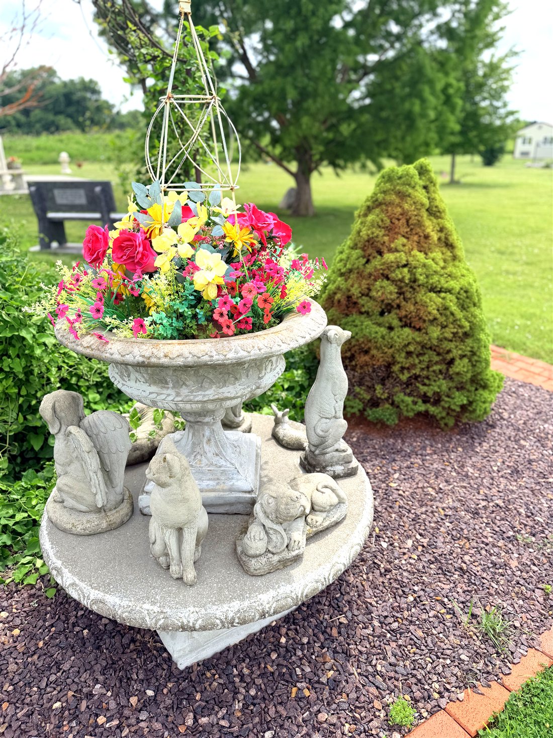 A memorial garden urn with flowers and small animal statues at the cemetery
